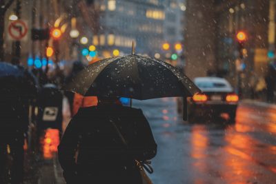 person walking down a darkened city street with an umbrella in the rain
